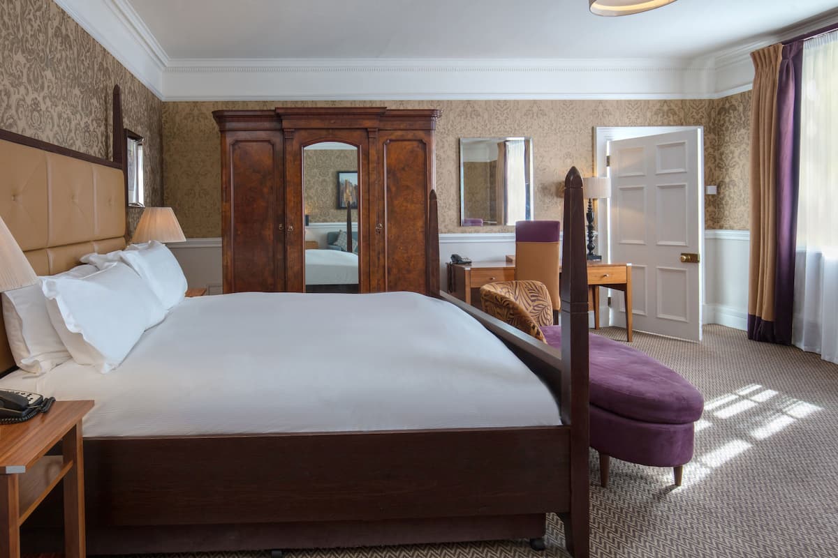 A hotel room with a large bed, a wooden wardrobe, a desk with a chair, and a mirror.