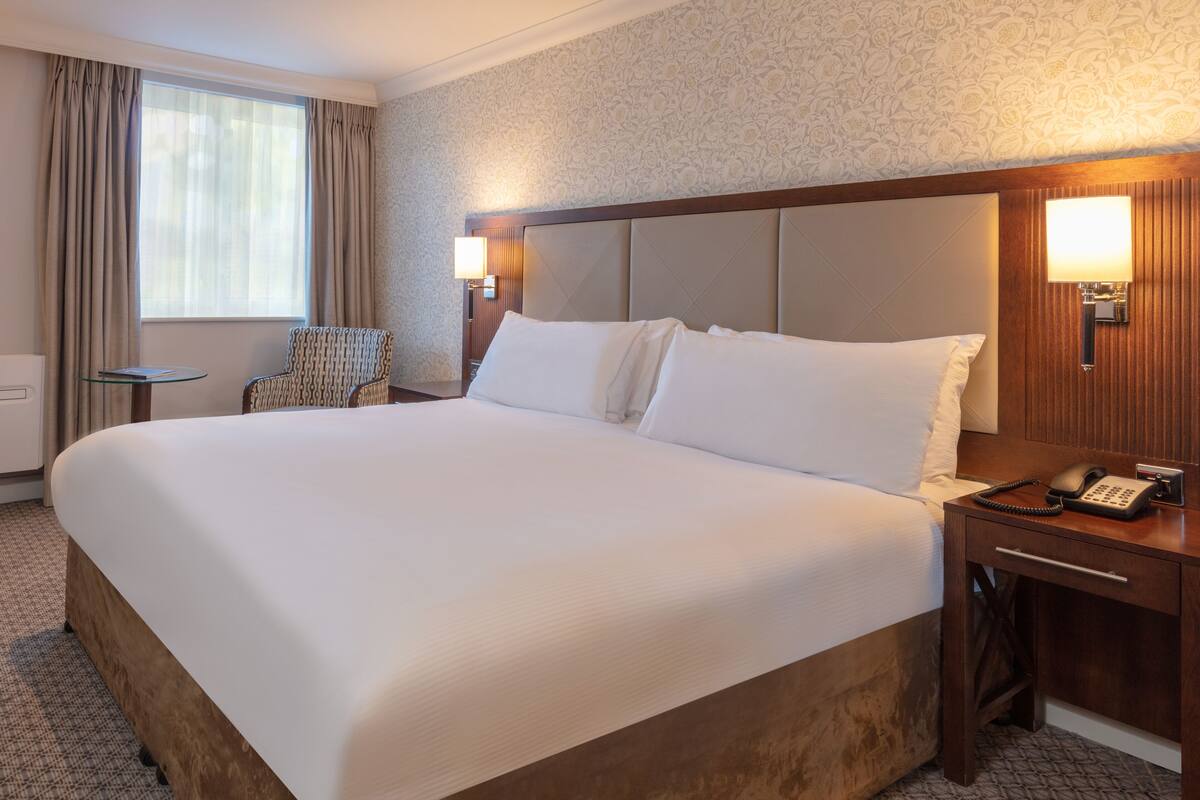 A hotel room with a large bed, a bedside table with a lamp, a chair, and a telephone.
