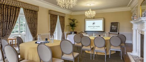 A conference room with a large oval table, multiple chairs, a chandelier, a projector screen displaying "Norton Park," and a fireplace.