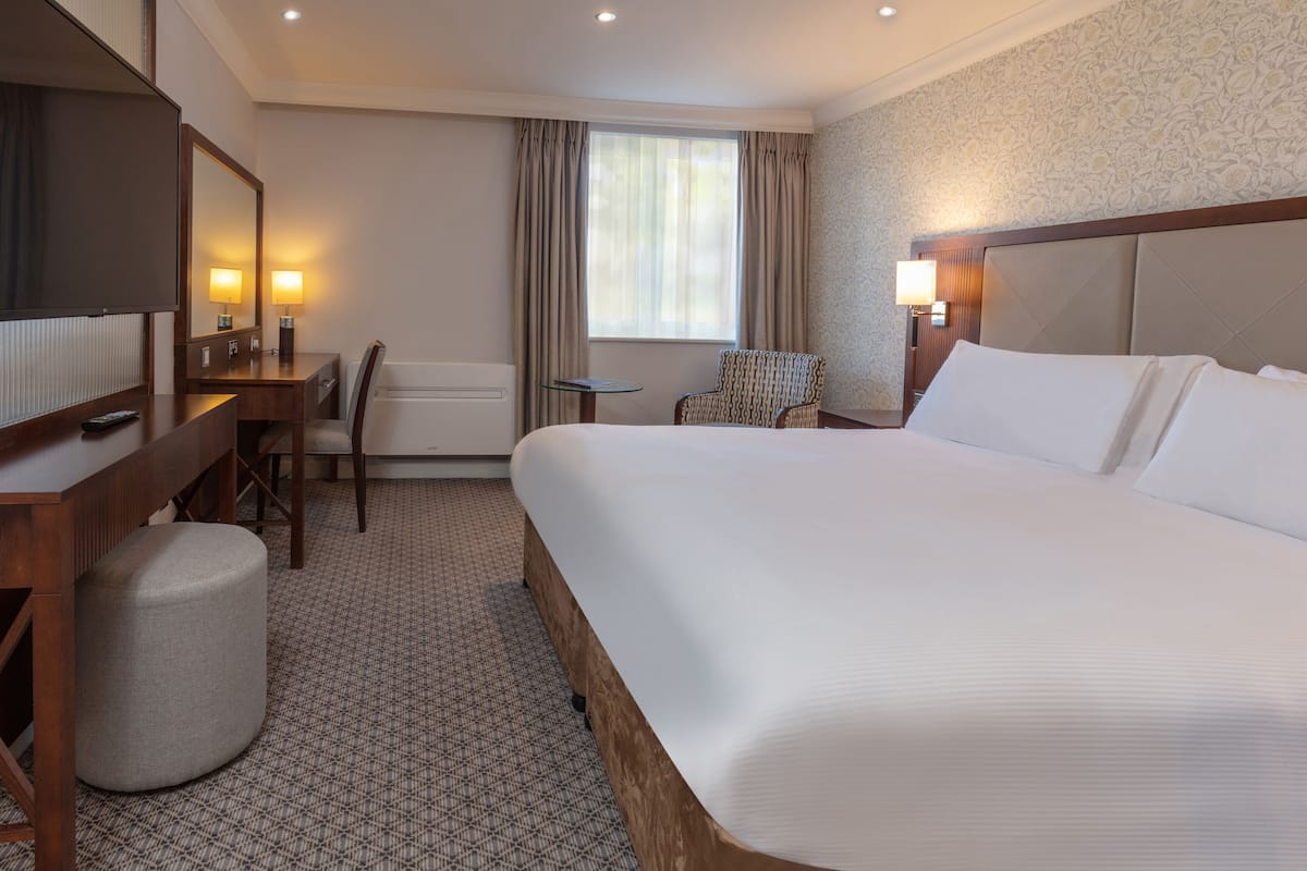 A hotel room with a large bed, a desk with a chair, a small table, a sofa, and a TV.