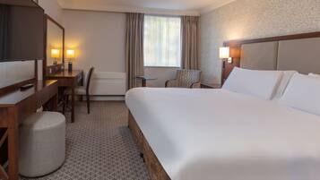 A hotel room with a large bed, a desk with a chair, a small table, a sofa, and a TV.
