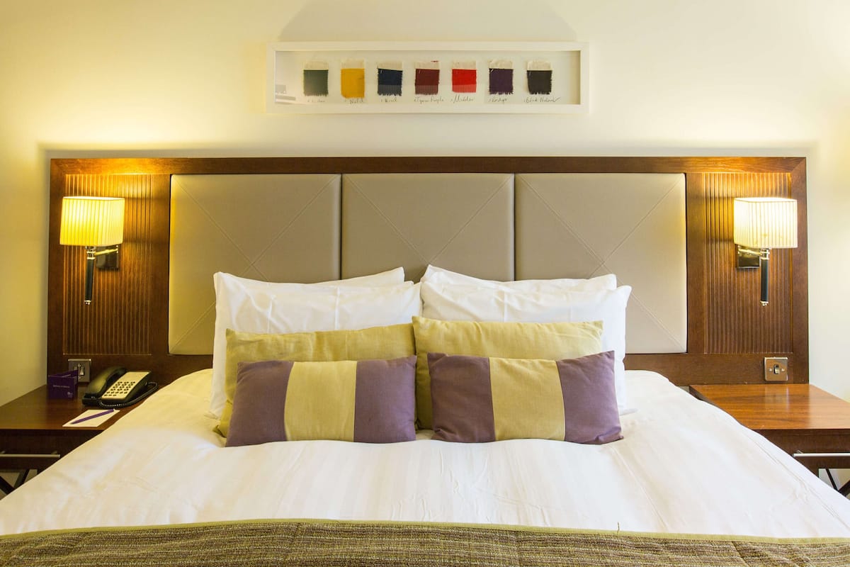 A hotel room with a large bed, two bedside tables, a wall-mounted color palette, and two wall-mounted lamps.
