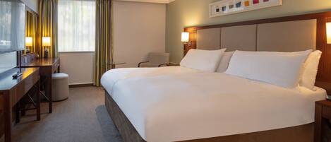 Una habitación de hotel con una cama grande, un escritorio con una silla, un taburete pequeño y un televisor.