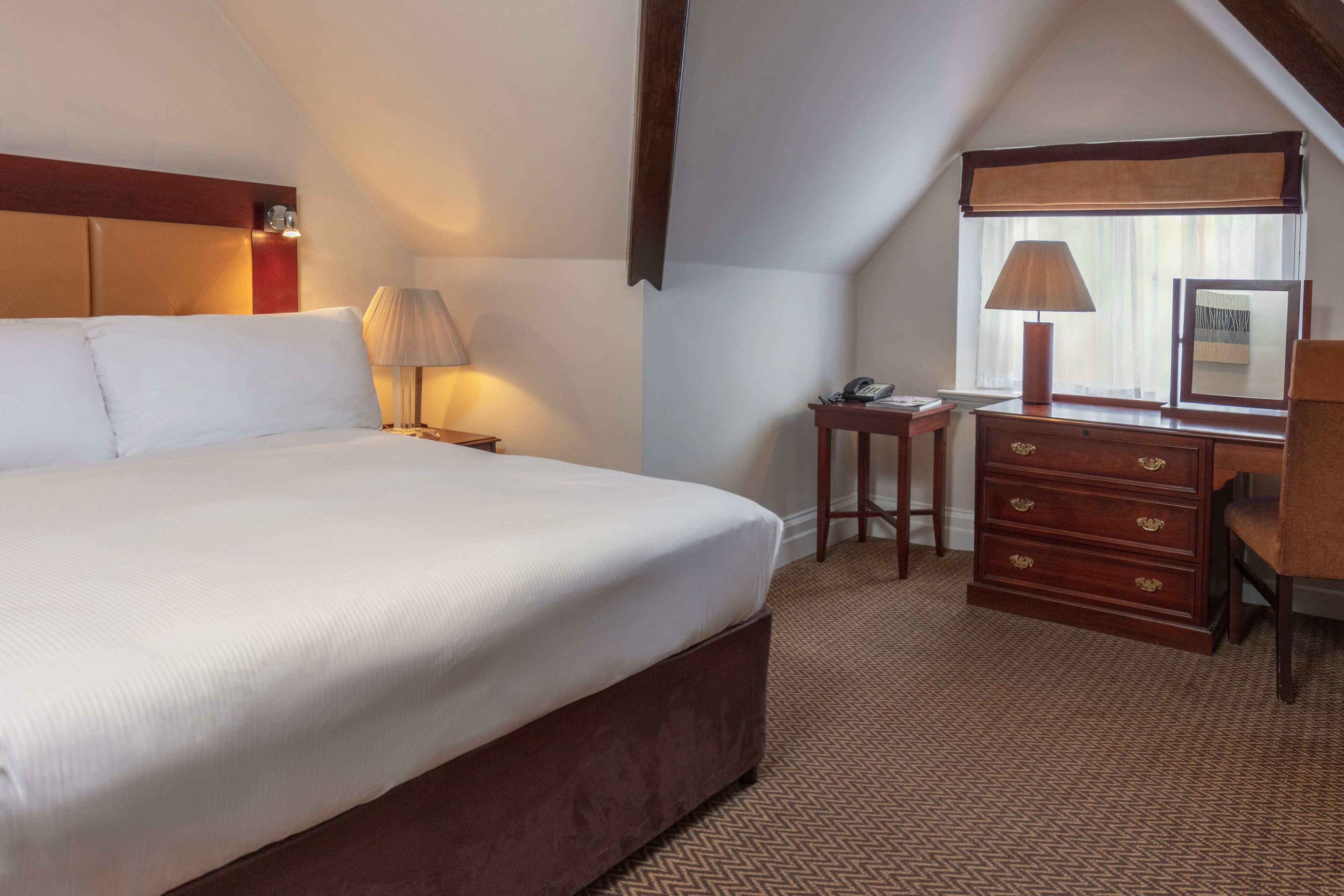 Une chambre d’hôtel avec un grand lit, un bureau avec une lampe et une commode.