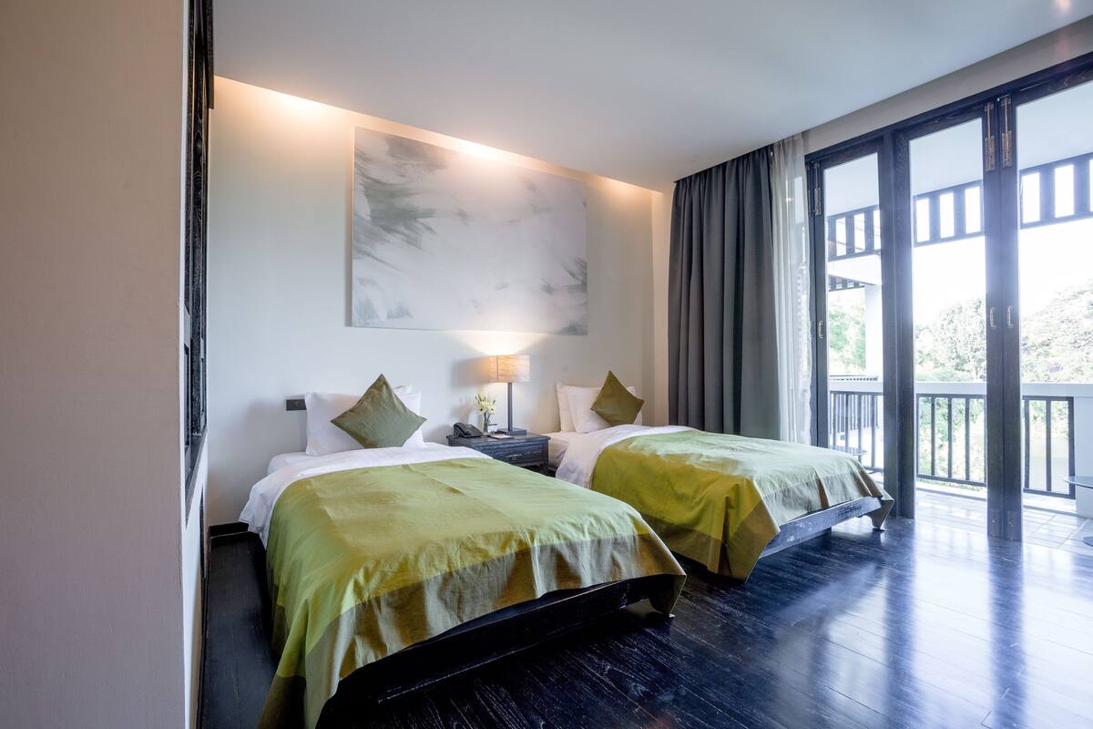 Habitación de hotel con dos camas, un ventanal grande y un balcón.
