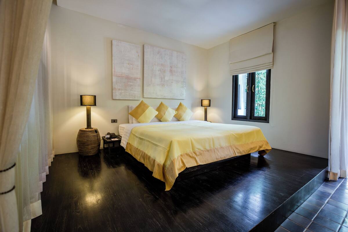 Un dormitorio con una cama grande, dos lámparas de noche, una ventana con persianas y una obra de arte en la pared.
