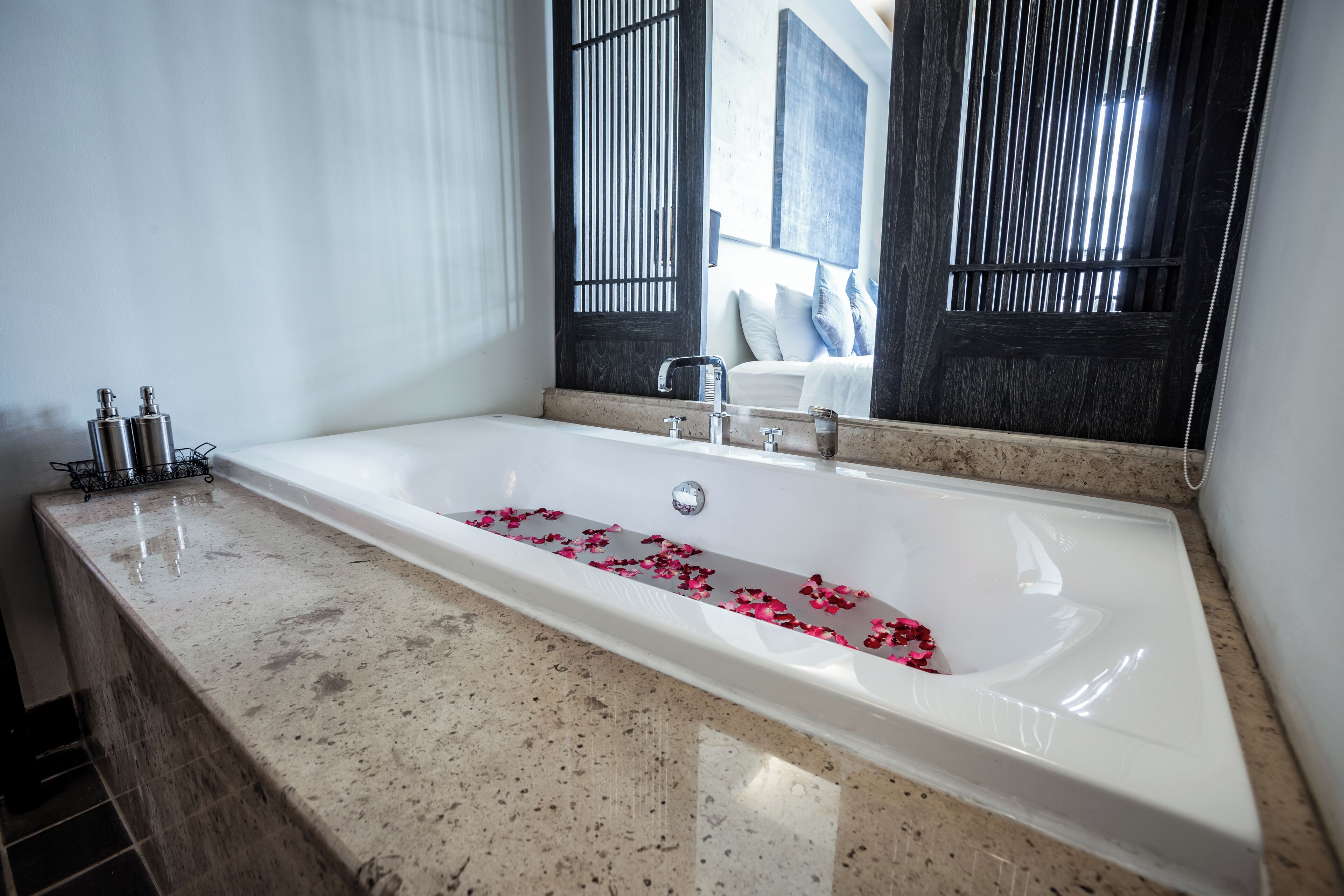 A modern bathroom with a large bathtub, a marble countertop, and a window with vertical blinds.