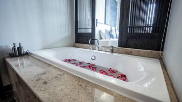 A modern bathroom with a large bathtub, a marble countertop, and a window with vertical blinds.