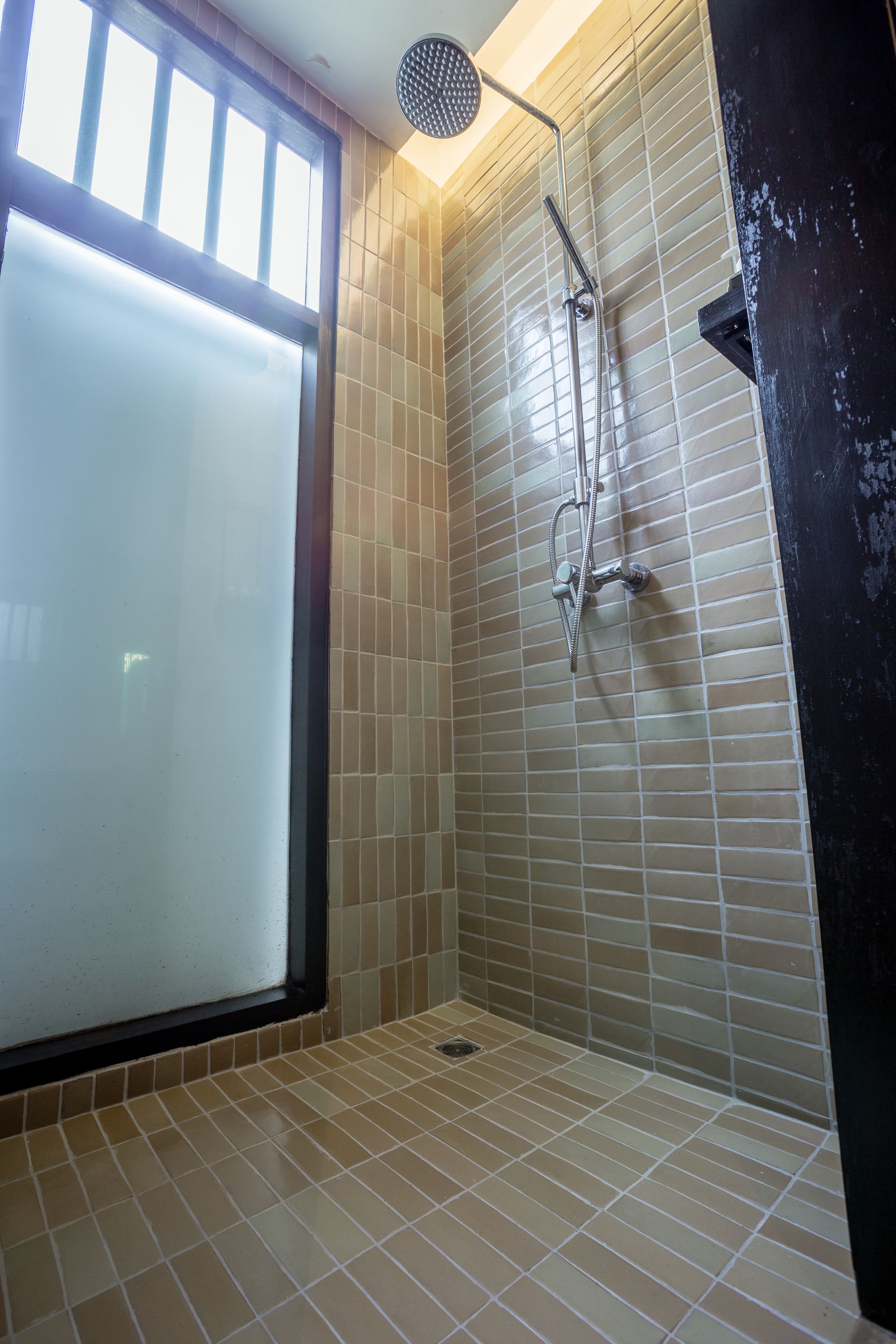Une salle de bain avec des carreaux de couleur beige, une douche et une fenêtre.