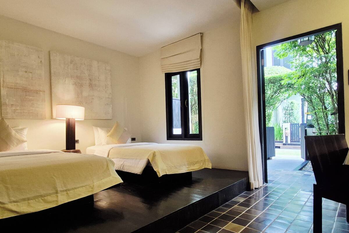 Habitación de hotel con dos camas, una ventana con vista a zonas verdes y una silla junto a la ventana.