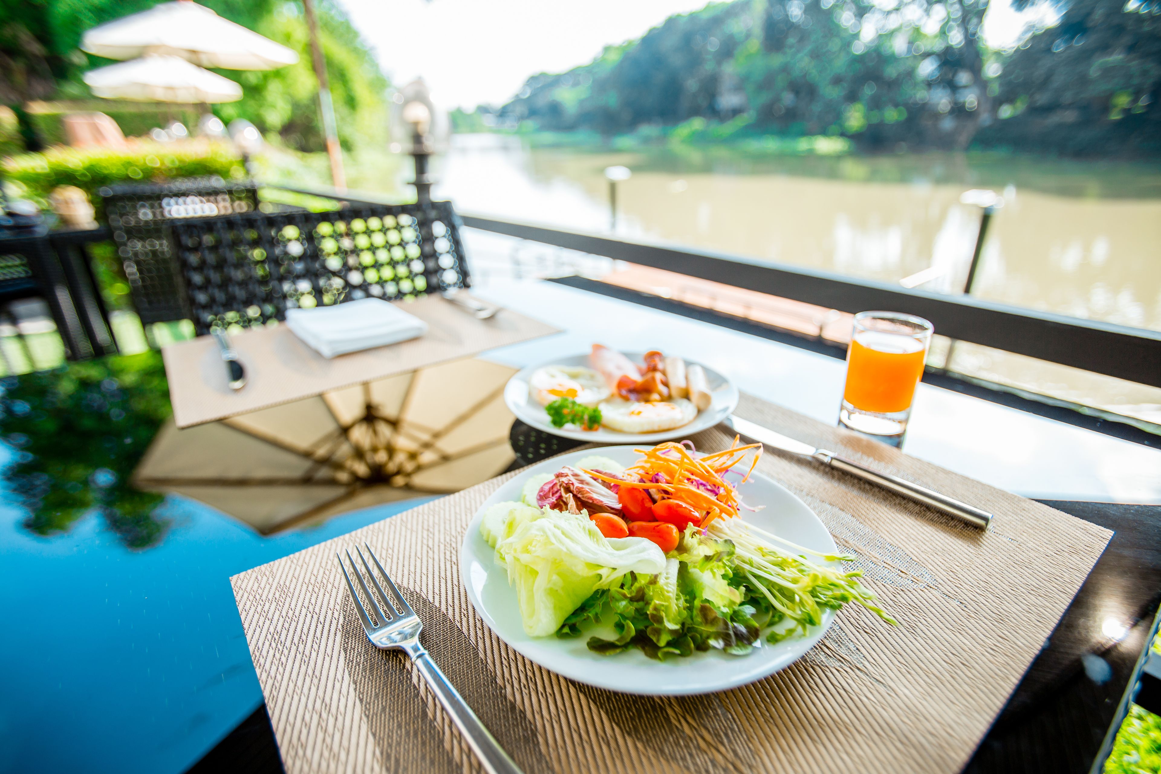 A dining table with a plate of salad and a glass of orange juice, overlooking a river.