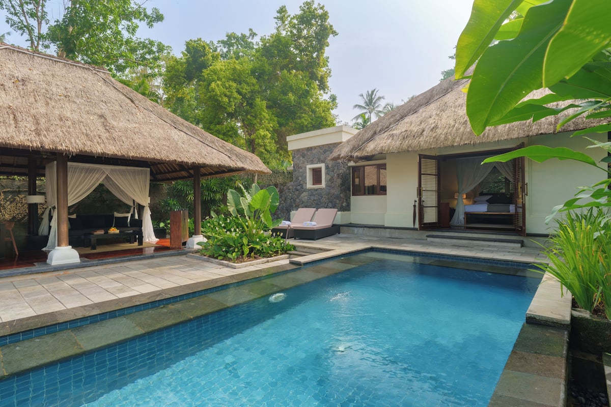 A pool area with thatched-roof structures, a stone building, and lush greenery.