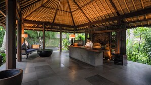 A reception area with a thatched roof, a reception desk, seating area, and large windows overlooking greenery. - Kayumanis Ubud Private Villas & Spa (Ubud)