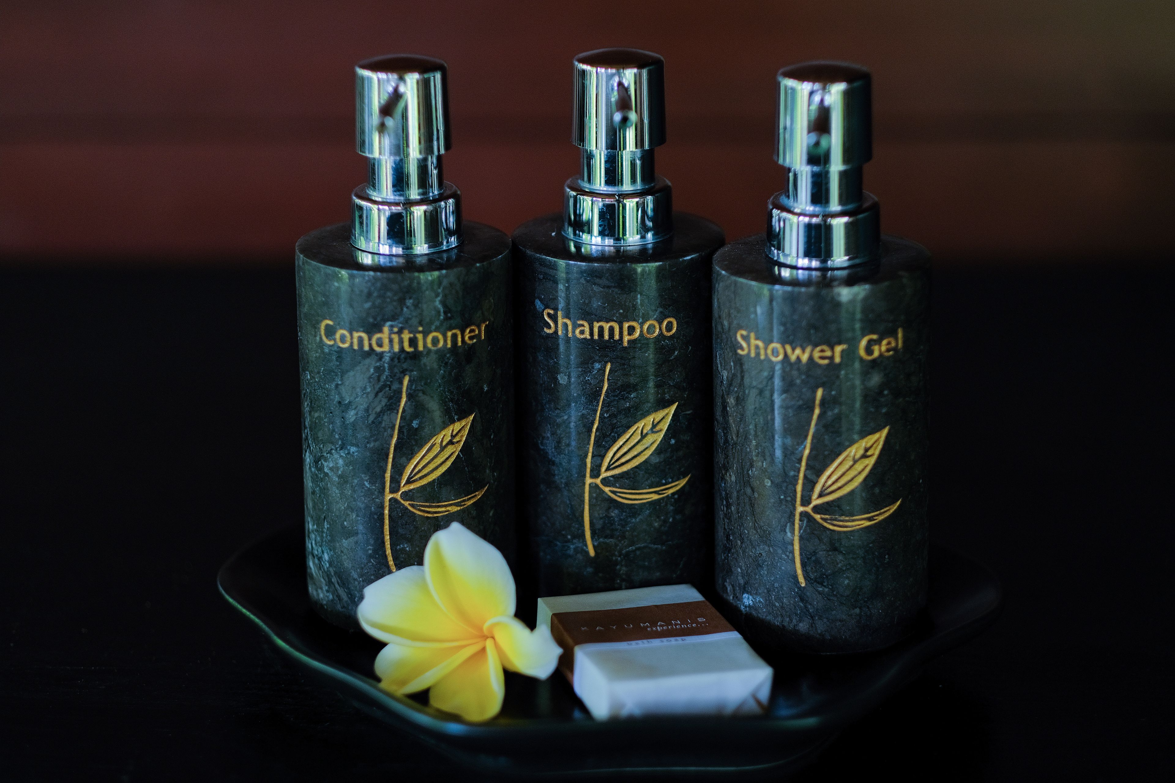 Three bottles of toiletries on a tray with a flower and a bar of soap.