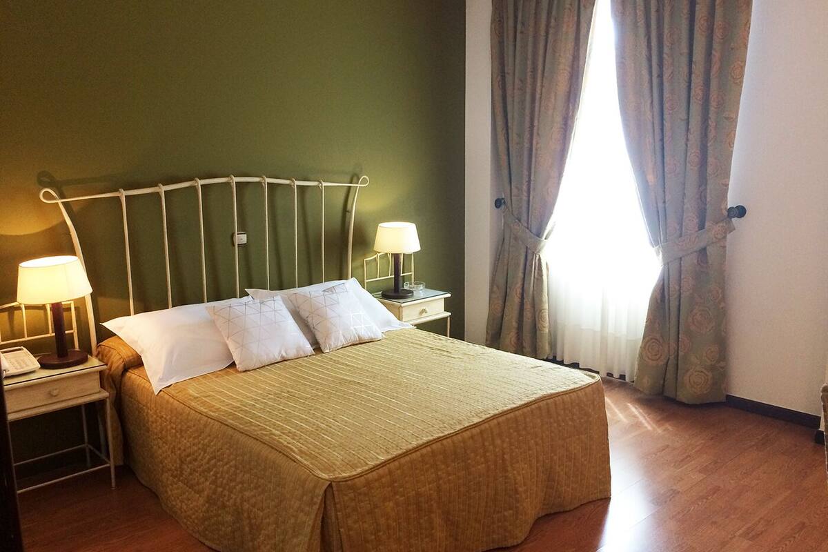 A neatly made bed with a headboard, two bedside lamps, and a nightstand with a telephone.