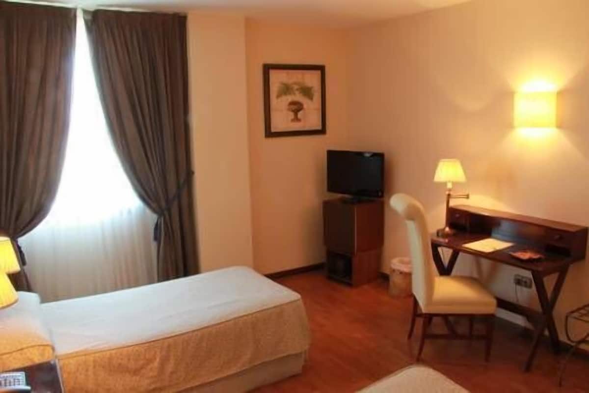 A hotel room with a bed, a desk, a chair, a television, and a lamp.