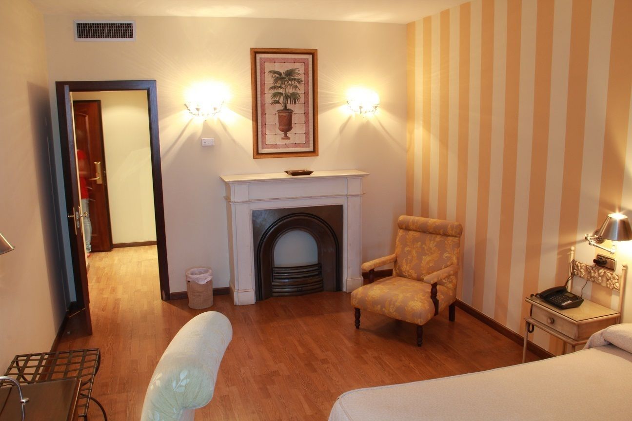 Habitación de hotel con chimenea, una silla, una cama, una mesita de noche y una pared con papel tapiz a rayas.