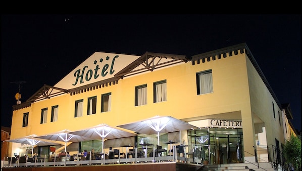 Un hotel con un letrero que dice 'Hotel', asientos exteriores con sombrillas y un letrero de 'CAFETERÍA'.