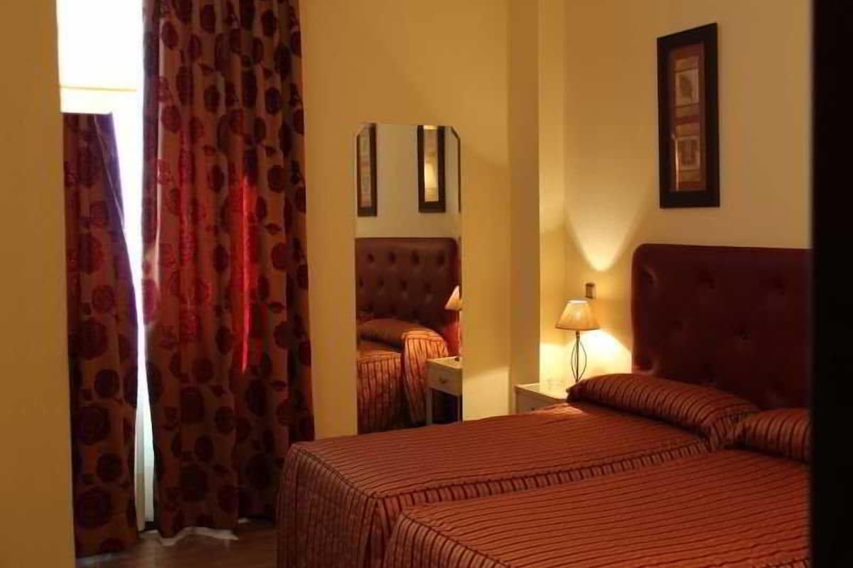 A hotel room with a large bed, a nightstand with a lamp, a mirror, and a framed picture on the wall.