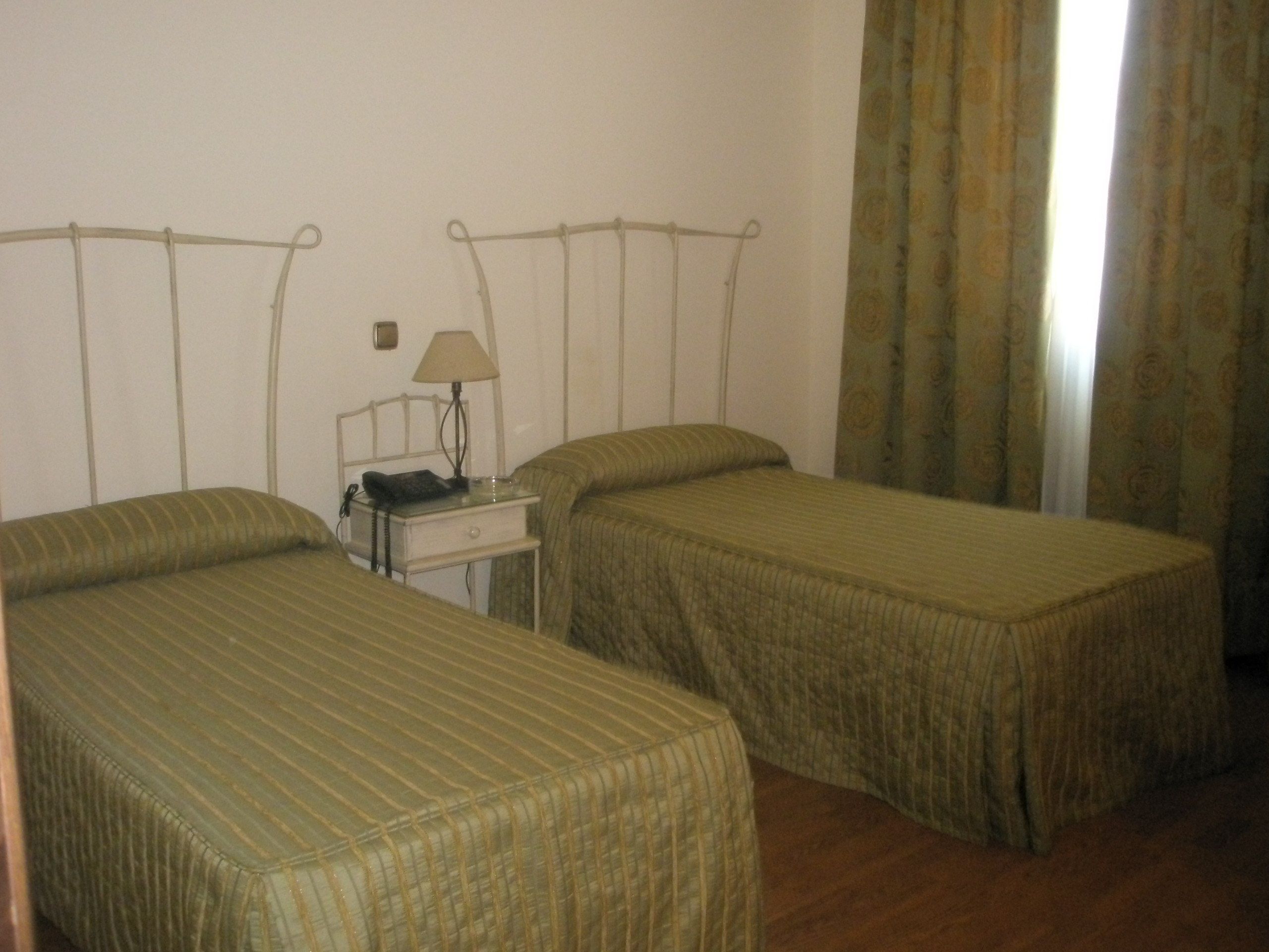Una habitación con dos camas individuales, una mesita de noche con lámpara y teléfono.