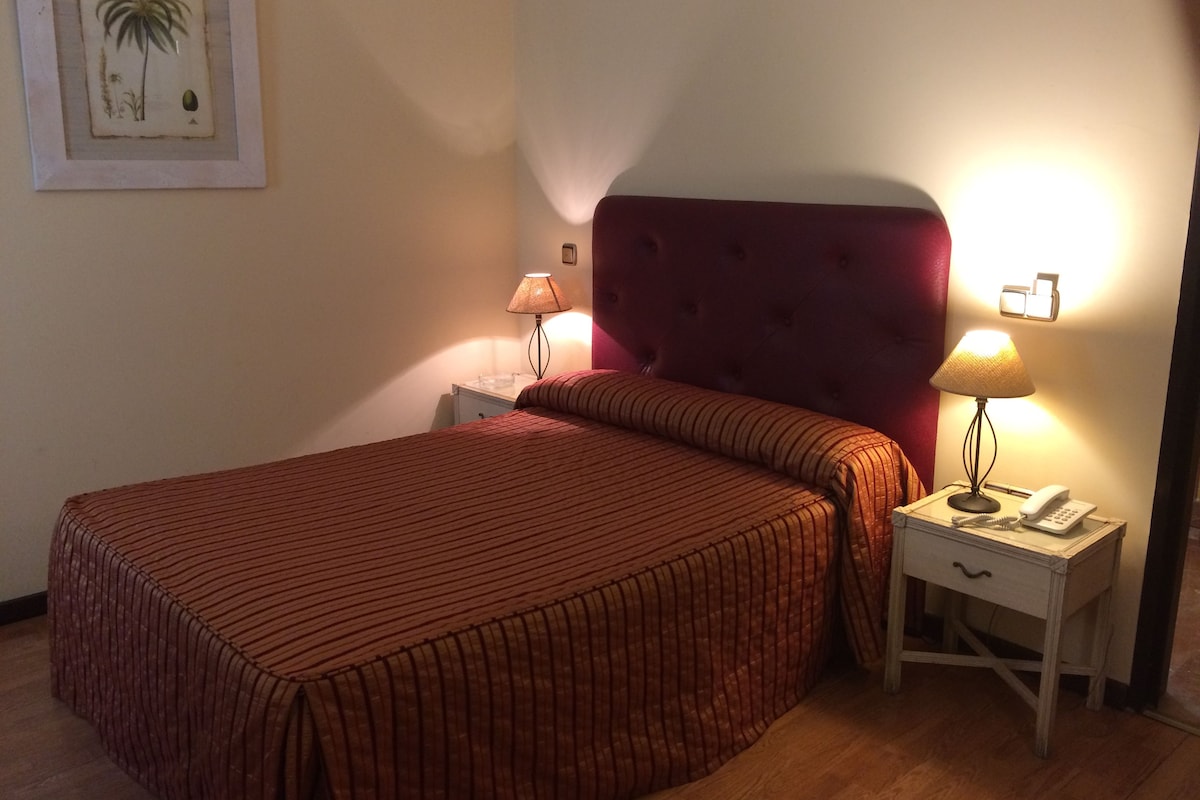 A hotel room with a large bed, two bedside tables, a nightstand, a lamp, and a framed picture on the wall.