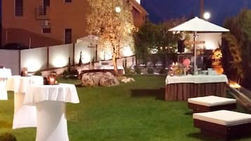 An outdoor patio area with tables and chairs, a small stage with a microphone, and a building in the background.