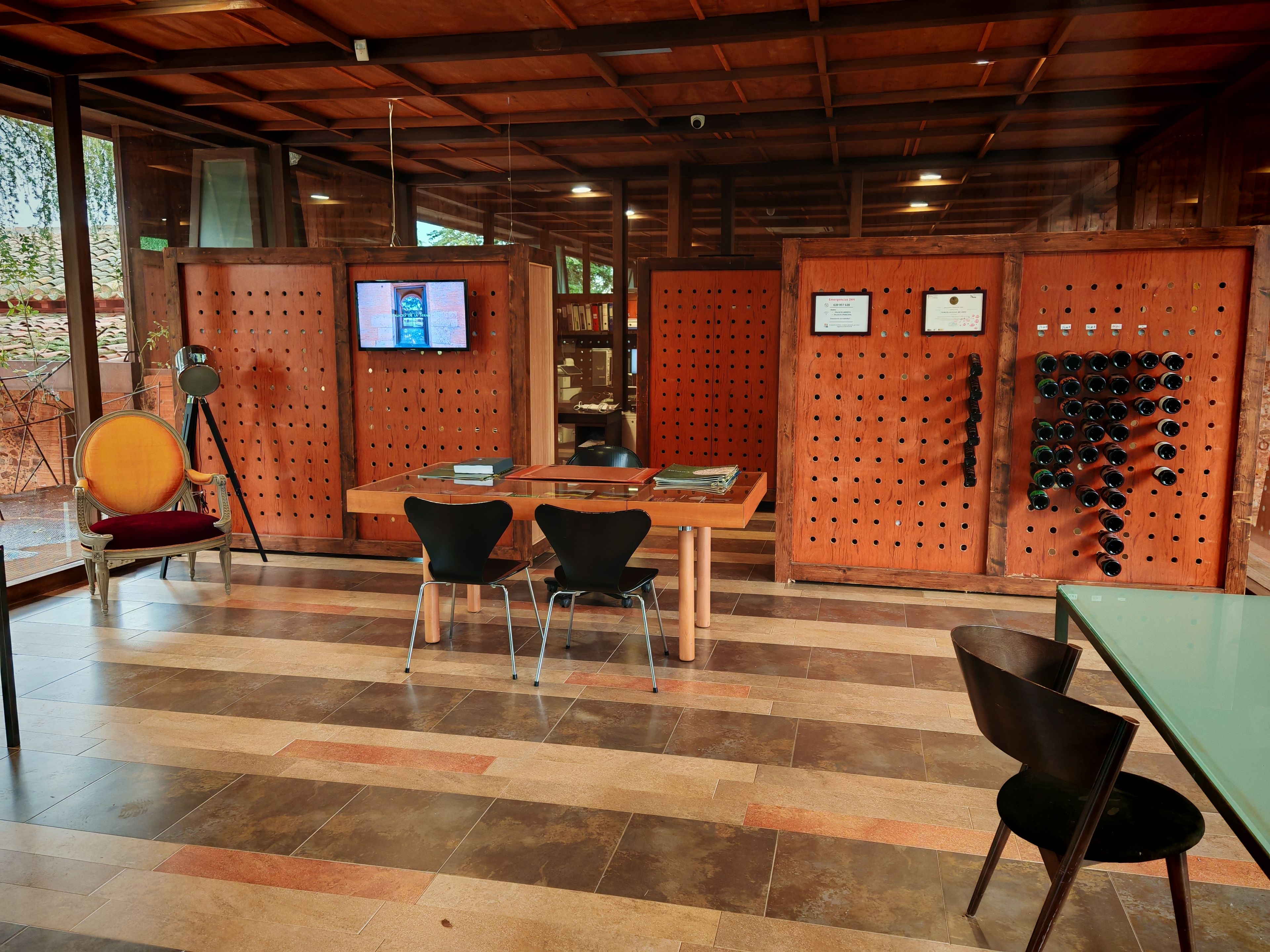 Un interior moderno con techo de madera, un televisor montado en un panel de madera, una mesa con sillas y una pared con un tablero de corcho.