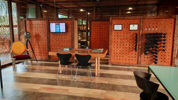 Un interior moderno con techo de madera, un televisor montado en un panel de madera, una mesa con sillas y una pared con un tablero de corcho.