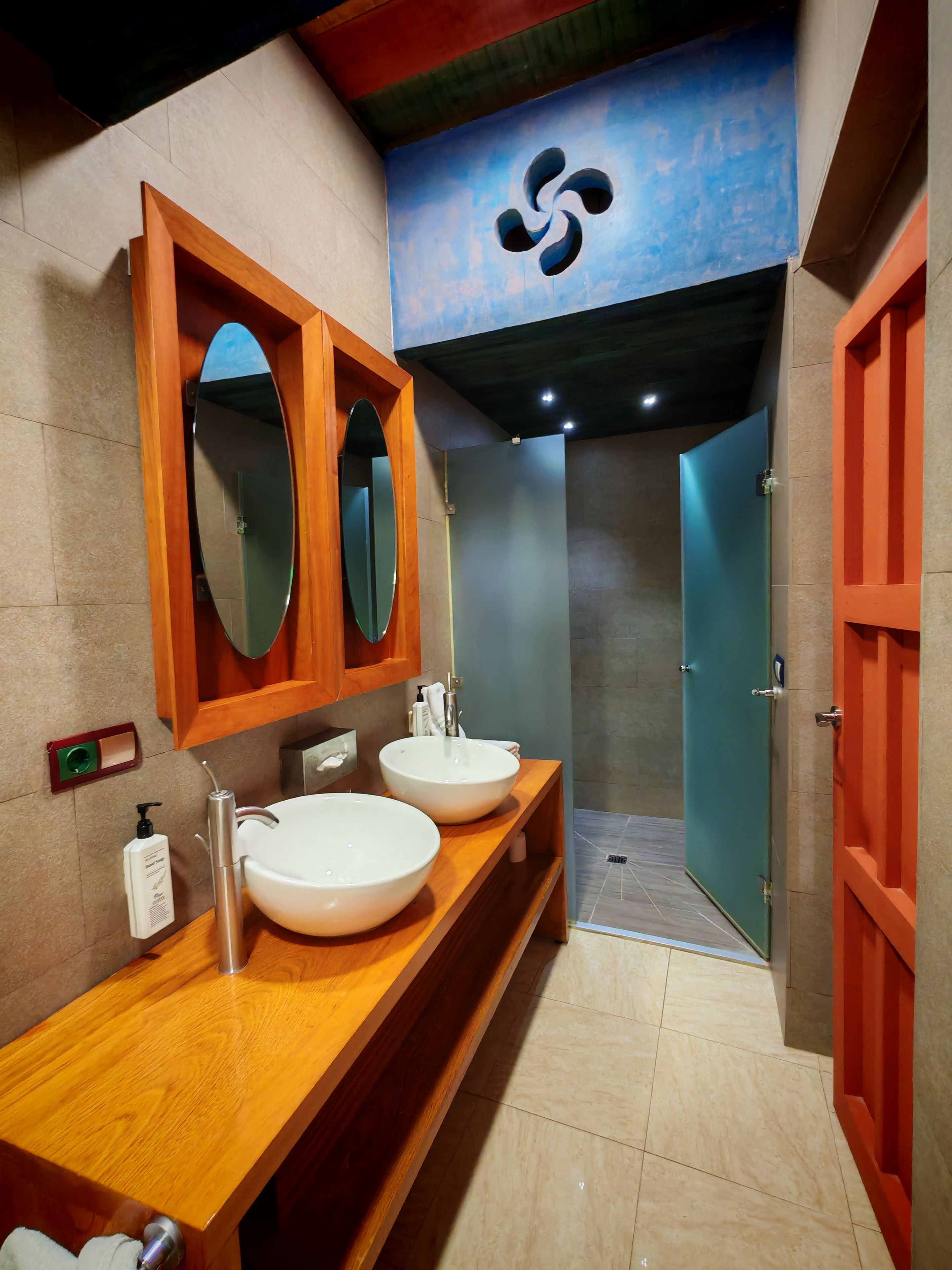 Un baño moderno con dos lavamanos grandes, un tocador de madera, un espejo y una zona de ducha.