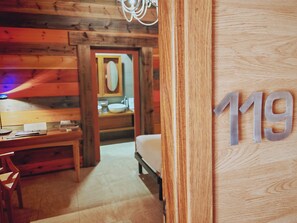 A wooden interior with a bed, a desk, and a bathroom visible through an open door. - Palacio de la Serna (Ballesteros de Calatrava)