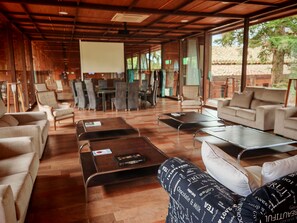 A spacious indoor area with wooden flooring, multiple seating arrangements including sofas and chairs, a coffee table, and a projection screen. - Palacio de la Serna (Ballesteros de Calatrava)