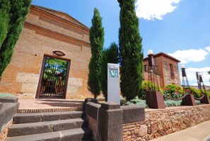 A building with a brick facade, a metal gate, and a sign indicating a palace. - Palacio de la Serna (Ballesteros de Calatrava)