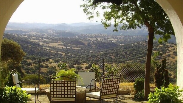 Une terrasse avec deux chaises et une table, d’où l’on peut admirer une vallée parsemée de vignobles et dominée par des collines lointaines.