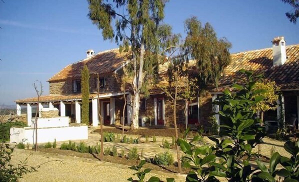 A traditional stone house with a tiled roof, surrounded by a garden with various plants and trees. - El Añadio (Vilches)