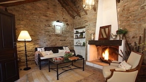 Une pièce chaleureuse avec un mur en pierre, une cheminée, un canapé, un fauteuil et une table avec une lampe.
