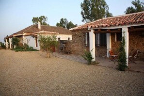 A stone house with a tiled roof, a gravel driveway, and a small patio with chairs. - El Añadio (Vilches)