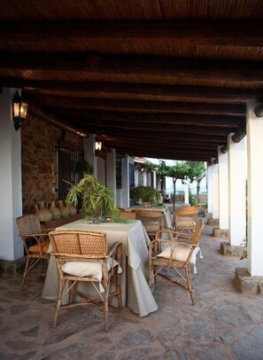 An outdoor dining area with wicker chairs and tables, stone flooring, and a stone wall. - El Añadio (Vilches)