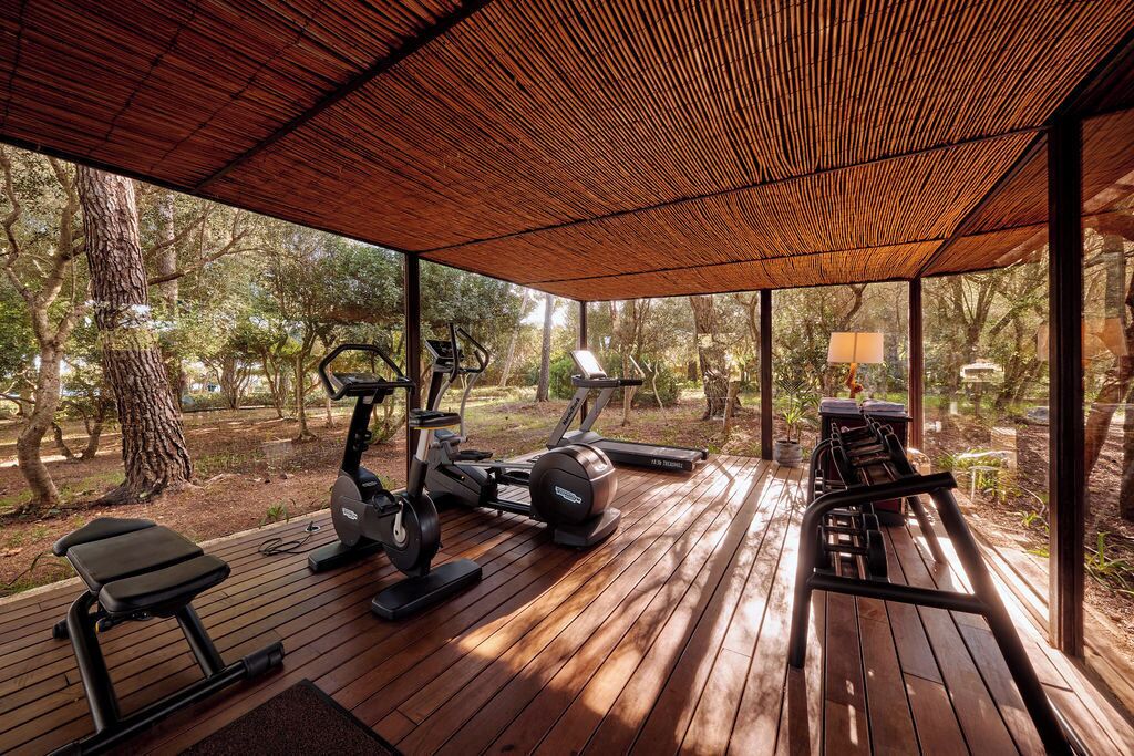 An outdoor gym area with exercise equipment, including treadmills and a bench, under a wooden pergola.
