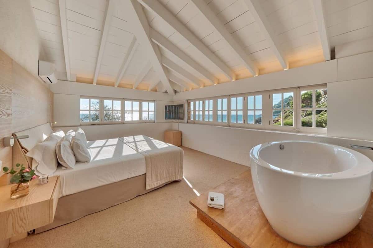 Un dormitorio moderno con una cama grande, una bañera amplia y vistas al mar.