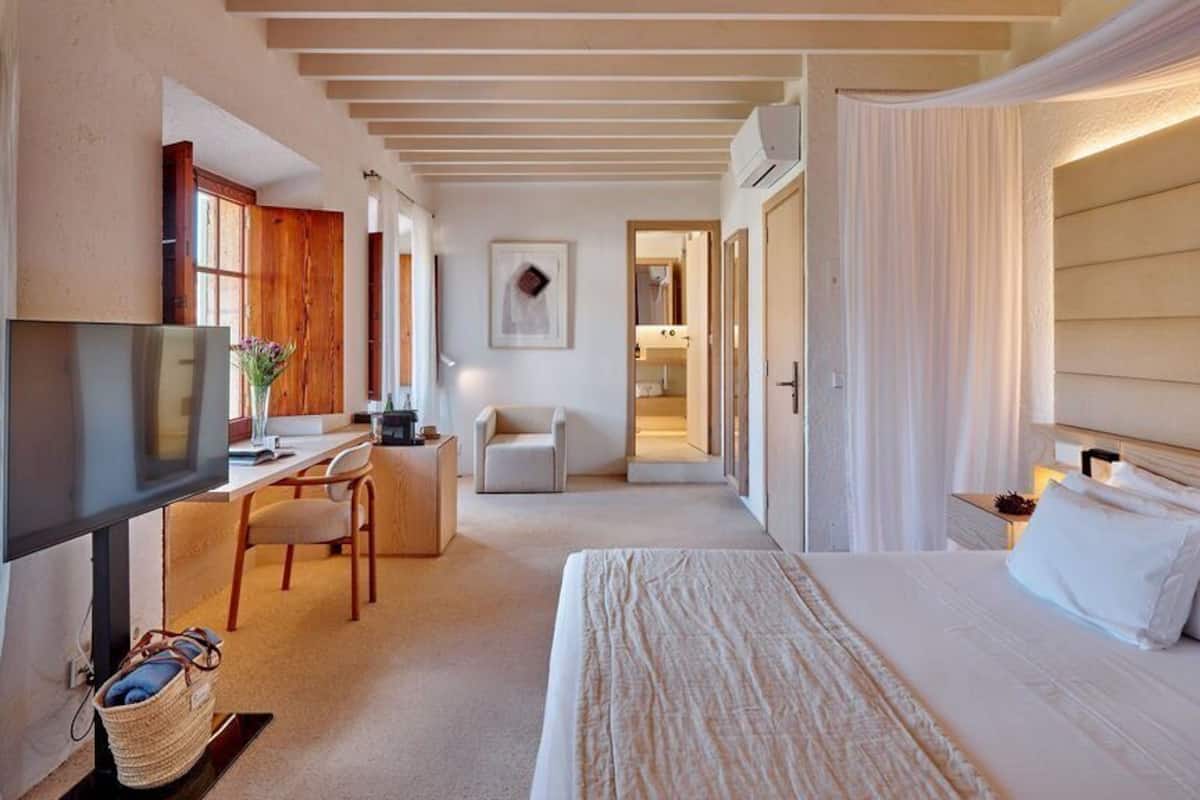 Habitación de hotel con cama, escritorio, silla, televisión y baño visible a través de una puerta abierta.