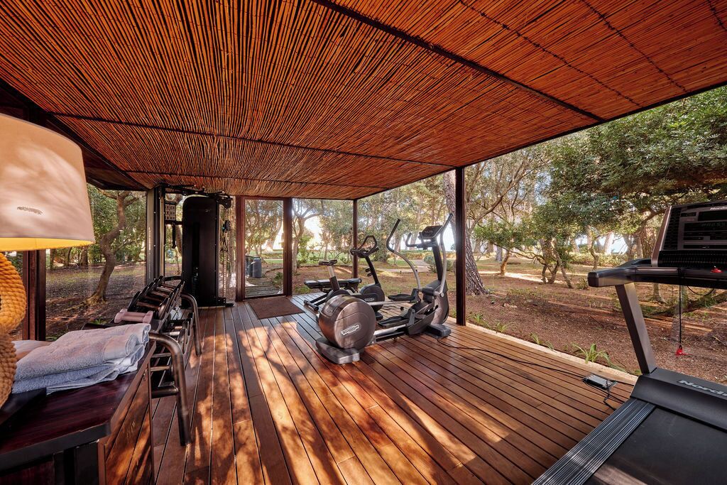 Un espacio exterior para gimnasia con equipo de ejercicio, una terraza de madera y una zona de estar cubierta.