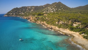 Un paisaje costero con aguas turquesas cristalinas, una playa arenosa y montañas al fondo.
