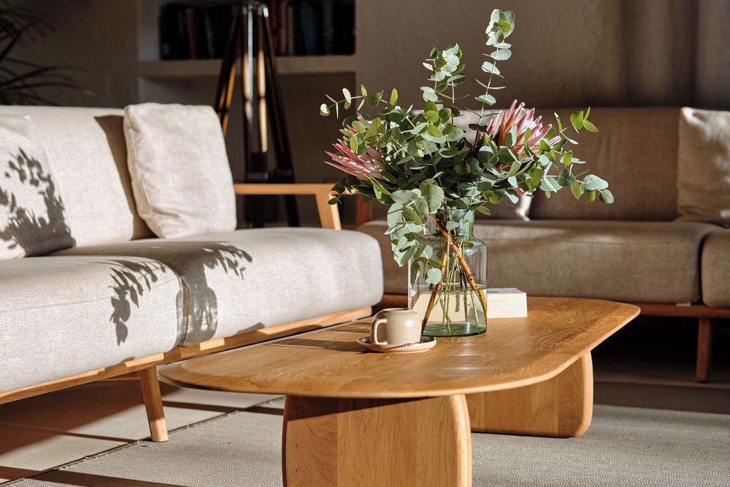 Una sala de estar moderna con un sofá, una mesa de centro de madera y un jarrón con flores.