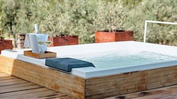 Een houten jacuzzi met een witte rand, een handdoek en een glas witte wijn op een houten terras.