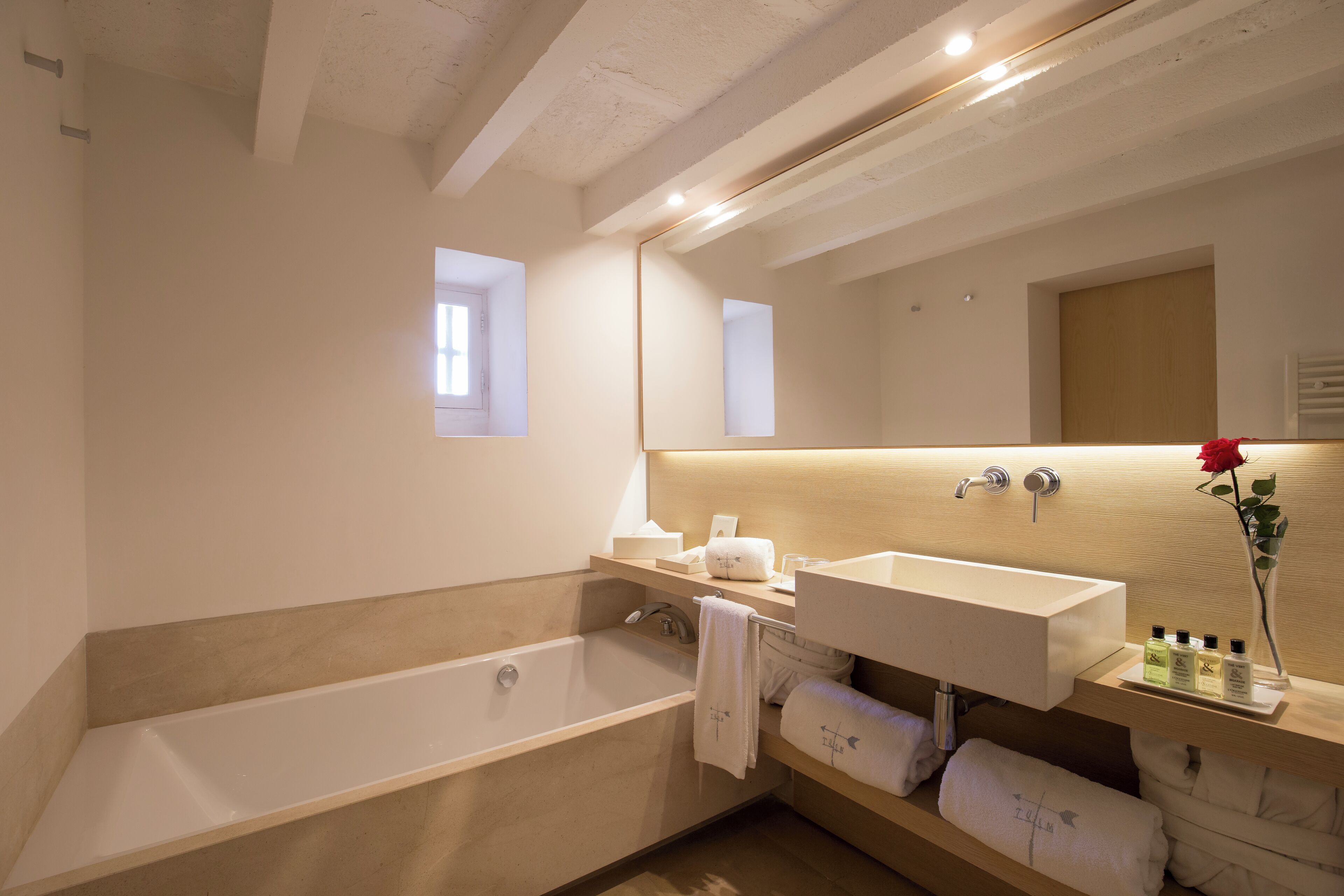 A modern bathroom with a bathtub, a large mirror, and a vanity with toiletries.