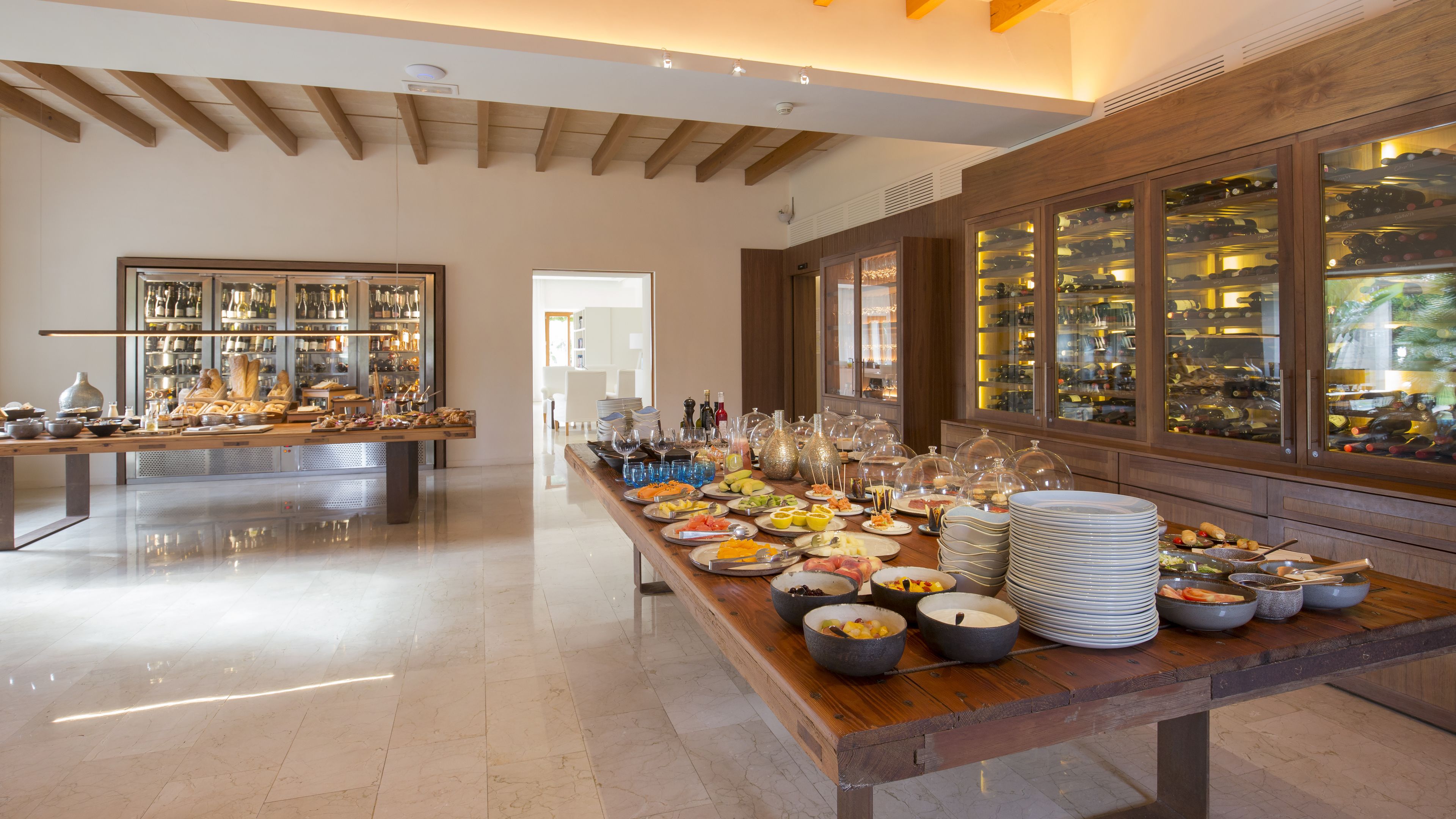 A spacious room with a long buffet table filled with various food items and a wine display.