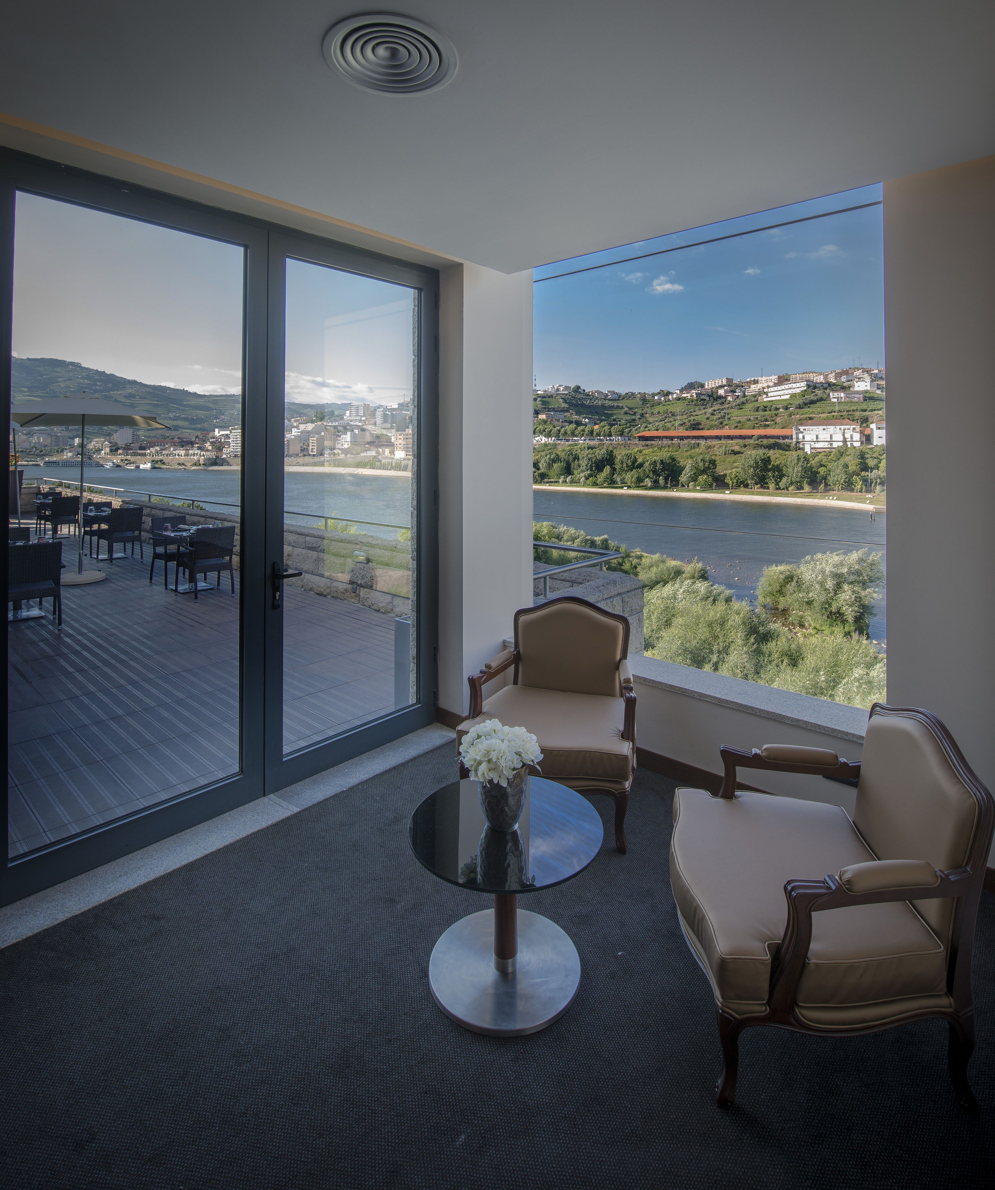 A balcony with a view of a river and distant buildings, furnished with a table and two chairs.