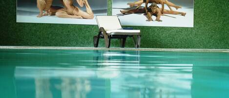 A swimming pool with a lounge chair and two large posters on the wall.