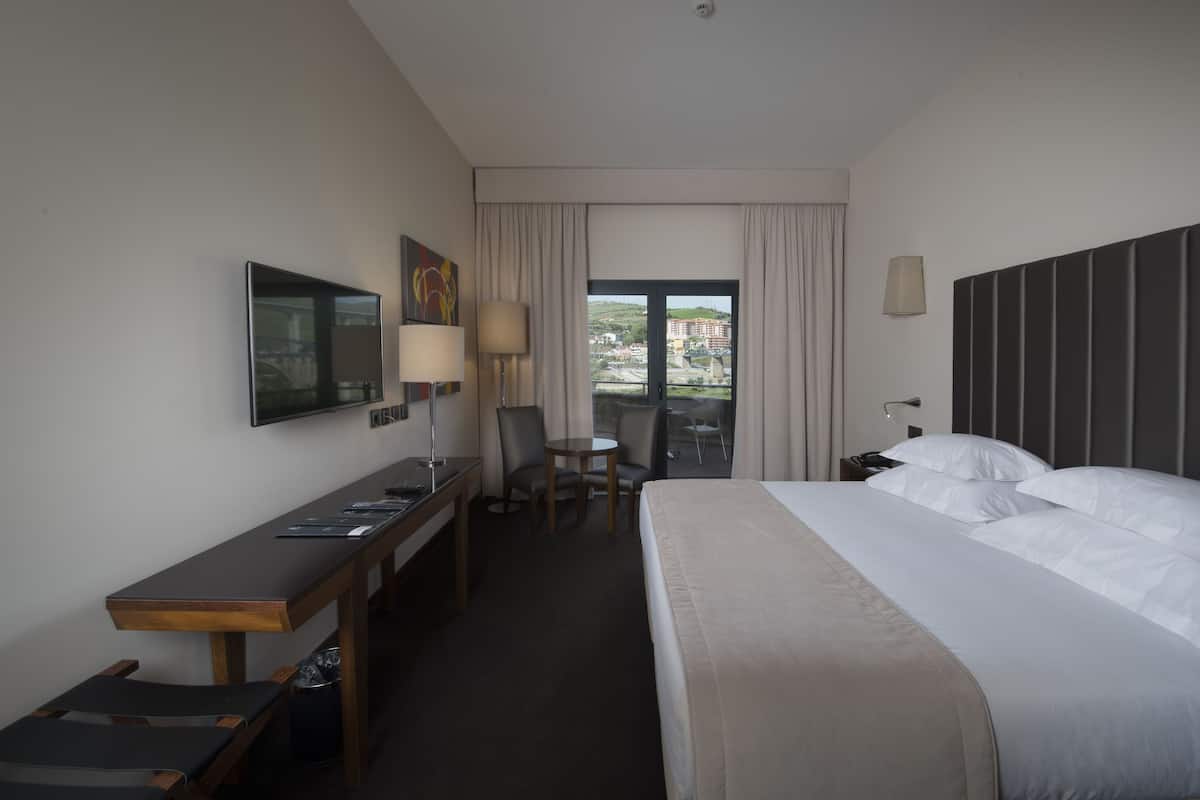 A hotel room with a bed, desk, chair, and a television.