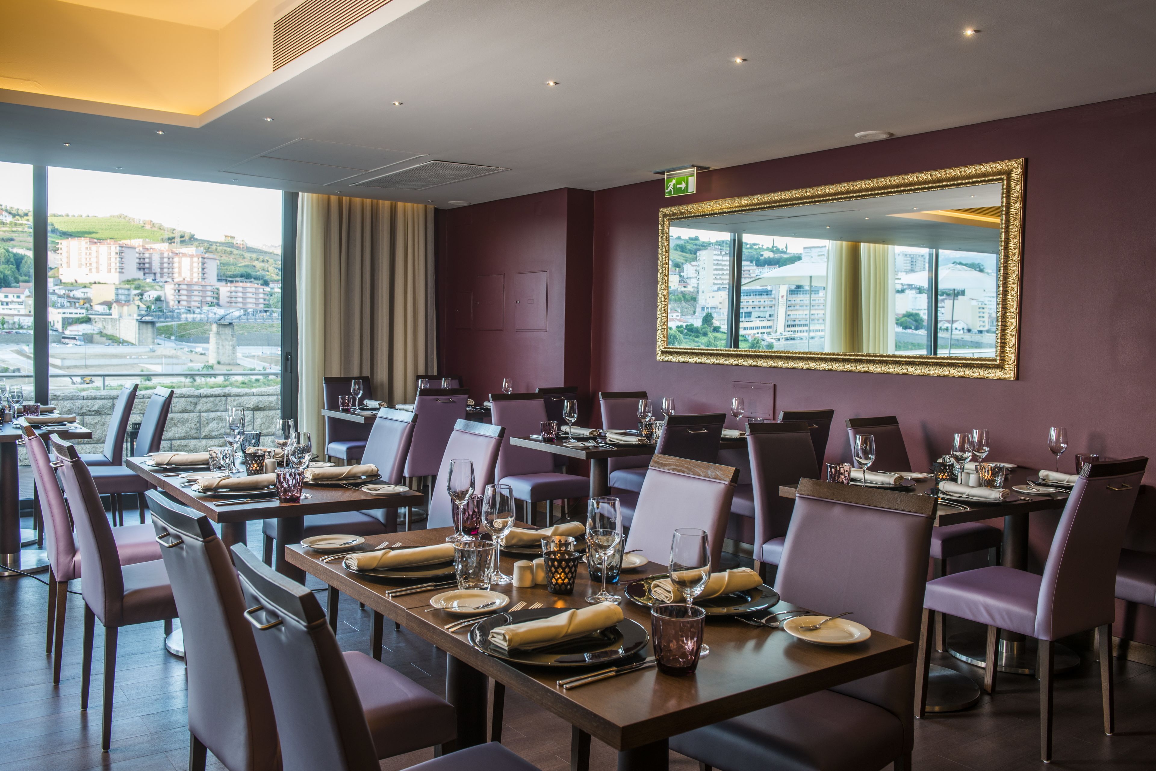 Un restaurante con mesas dispuestas para comer, un espejo grande en la pared y vistas a edificios a través de amplias ventanas.